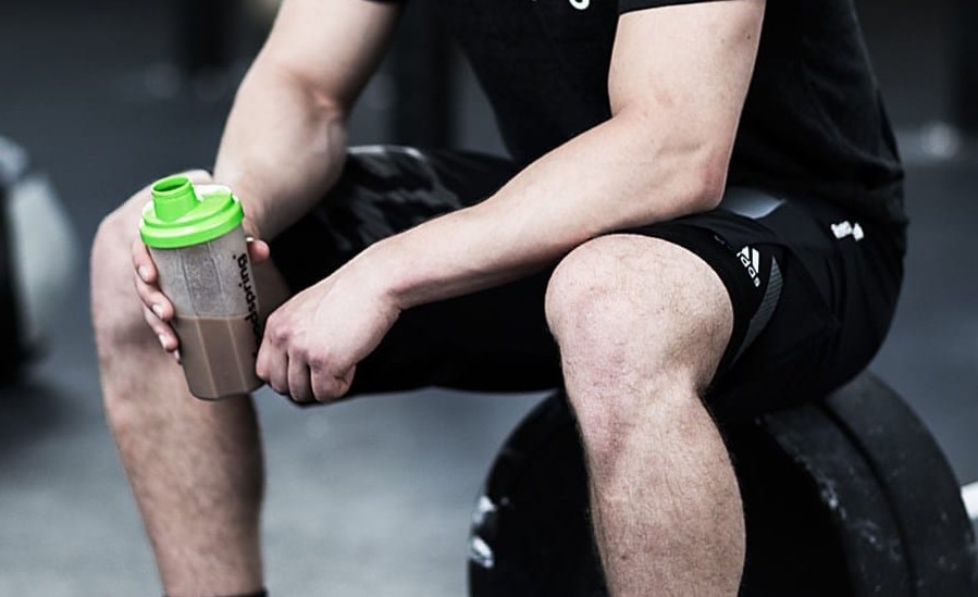 Sportif en salle de sport avec un shaker de Whey protéiné la main